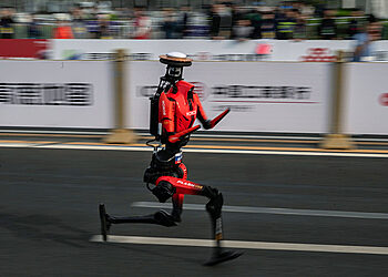 BEIJING, CHINA - APRIL 19: The fastest humanoid robot, an H1made by Honor, runs beside human runners at the start on its way to winning the Beijing Humanoid Half Marathon on April 19, 2026 in Beijing, China. The robot finished with a net time of 50 minutes and 26 seconds. More than 100 humanoid robots from 76 institutions across China lined up alongside 12,000 human runners Sunday in Beijing's E-Town district for the world's largest humanoid robot half-marathon, following the same 21-kilometre course on separate lanes in a 'human-robot co-running' format that for the first time included teams competing under fully autonomous navigation. (Photo by Kevin Frayer/Getty Images)