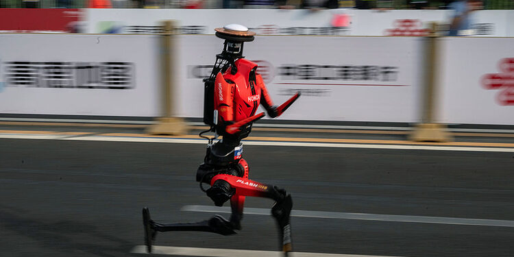 BEIJING, CHINA - APRIL 19: The fastest humanoid robot, an H1made by Honor, runs beside human runners at the start on its way to winning the Beijing Humanoid Half Marathon on April 19, 2026 in Beijing, China. The robot finished with a net time of 50 minutes and 26 seconds. More than 100 humanoid robots from 76 institutions across China lined up alongside 12,000 human runners Sunday in Beijing's E-Town district for the world's largest humanoid robot half-marathon, following the same 21-kilometre course on separate lanes in a 'human-robot co-running' format that for the first time included teams competing under fully autonomous navigation. (Photo by Kevin Frayer/Getty Images)